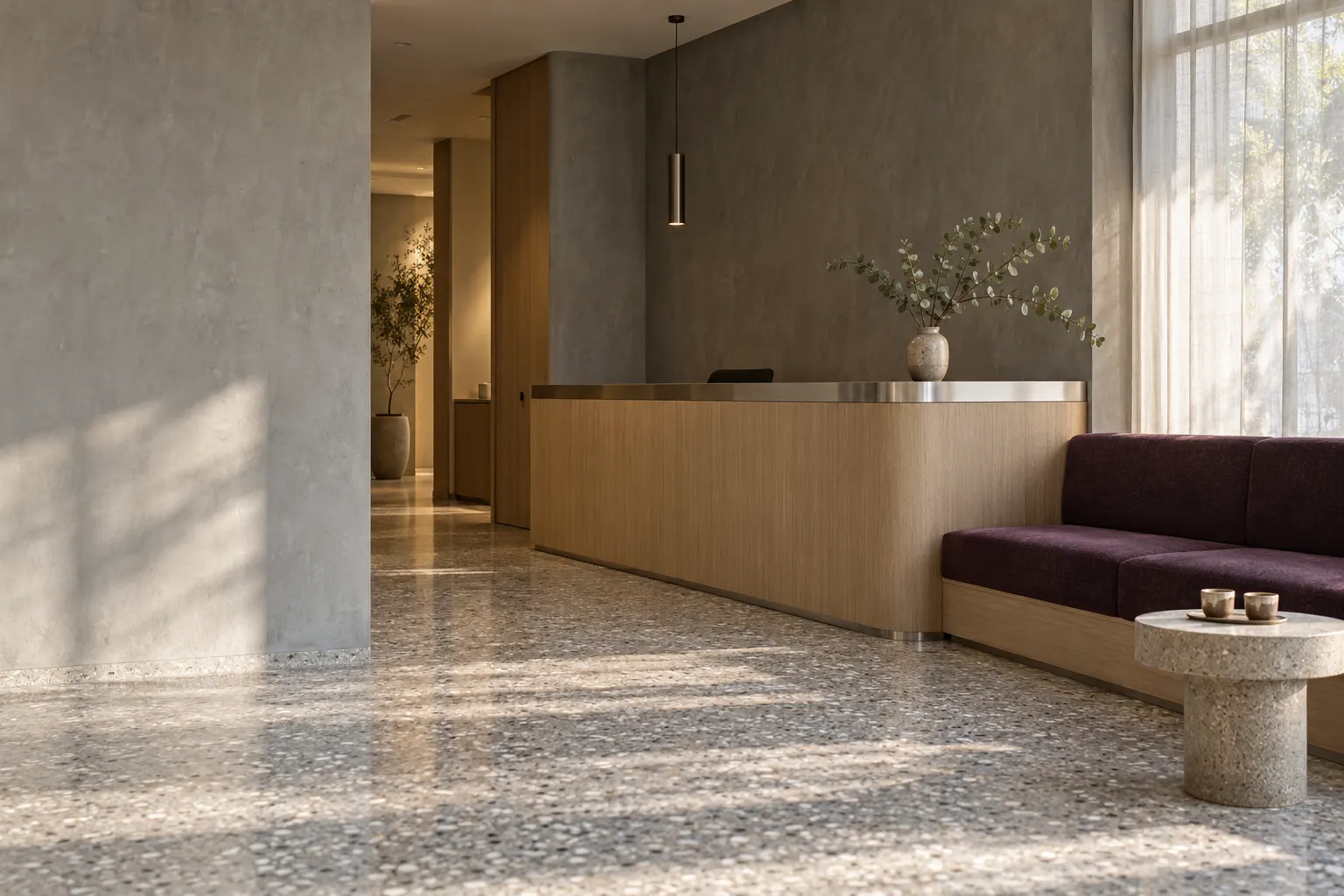 The reception lounge: a pale oak counter, a plum bench against grey plaster, morning light through linen